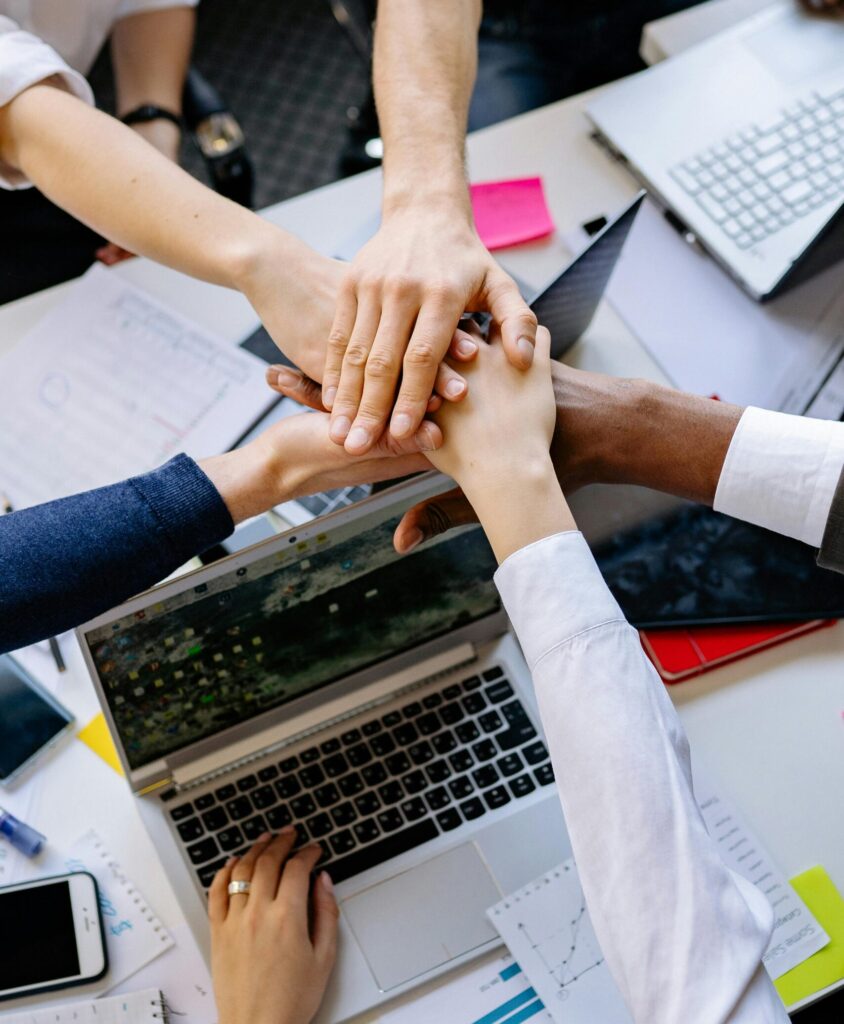 A diverse group of professionals stacking hands over a table symbolizing teamwork and collaboration.