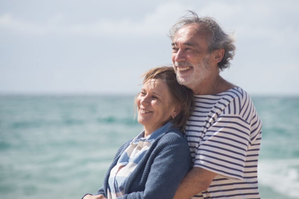 Happy senior couple embracing each other by the ocean, enjoying a sunny day in Portugal.