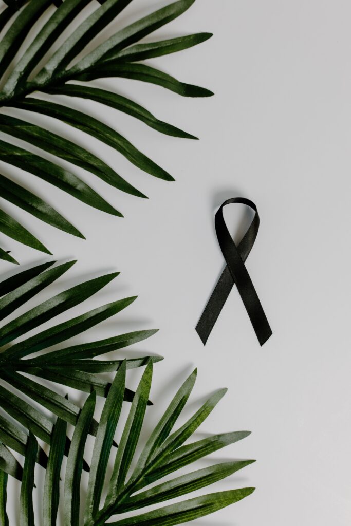 Black ribbon alongside green palm leaves on white background symbolizes mourning and cancer awareness.